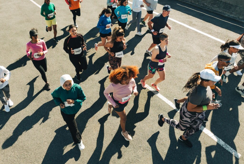 An overhead view of a diverse group of runners wearing race bibs competing in an outdoor road race on a sunny day.