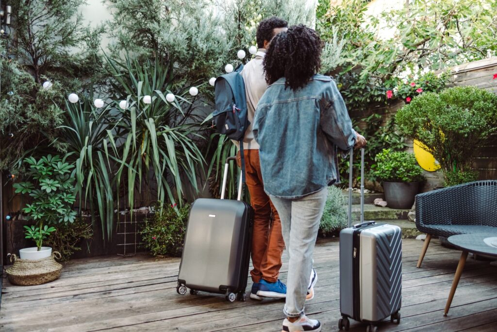 Couple rolls luggage on a garden path with string lights